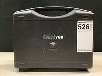 Closed black OmniVox branded hard plastic carrying case with handle and auction lot label on front
