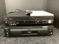 Panasonic DVD recorder stacked on top of Sony DVD player with remote and manuals on top