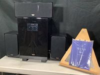 All components displayed: subwoofer, center, two bookshelf speakers, paperwork on wooden stand.