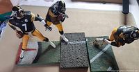 Three Steelers McFarlane football figures posed on football field bases, showing overall view of lot
