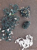 Five sets of Christmas lights laid out on pavement; four sets have green cords and one set has a white cord.