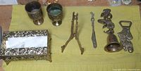 Photo showing the assortment of seven brass items including bell, tissue box holder, plate stand, spoon, and bottle openers