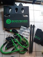 BodyBoss Total Workout System components laid out including base, resistance bands with handles, detachable bars, manual, and carrying bag.