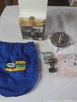 Primus Classic Trail camp stove parts displayed including blue carrying pouch, stove burner with control valve, original box and instruction manual.