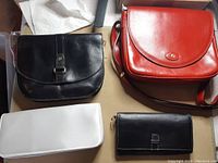 Four leather items on a table: red and black purses, white purse, and black leather wallet.
