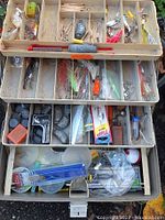 Top view showing three tiers of the fishing tackle box with multiple compartments containing a variety of fishing lures, weights, hooks, and accessories.