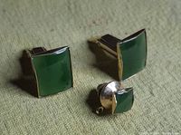 Pair of rectangular green stone cufflinks and single square tie tack set against a textured fabric background.