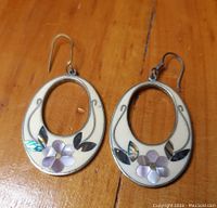 Front view of oval silver earrings with cream background decorated with inlaid flowers and abalone leaves.