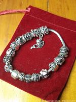 Full view of sterling silver charm bracelet arranged in circle, showing various detailed charms, displayed on a red velvet pouch.