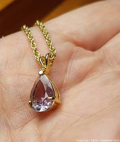Front view of gold-toned chain with pink teardrop faceted stone pendant held in prong setting on hand.