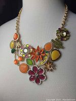 Front view of colorful floral maximalist necklace featuring multiple flower and leaf designs with orange, yellow, green, pink, purple stones, and gold-tone metal chain.