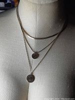 Photo of two gold-tone herringbone style necklaces and two pendant necklaces on a dress form.