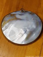 Back side of large round abalone pendant with smooth polished mother-of-pearl surface.