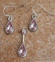 Pink stone teardrop pendant and matching earrings on a textured background.