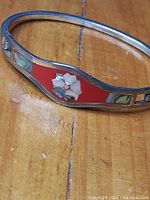 Close-up showing the rigid silver-tone bracelet with a bright red enamel or resin inlay centered with an abalone shell flower and smaller abalone shell inlays along the sides.