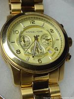 Close-up photo of the gold tone Michael Kors wristwatch face showing chronograph subdials, date display, and branding.
