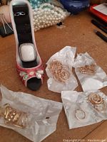 Photo showing pink high heel shoe ring holder containing two rings including a white square ring, and multiple new gold-tone rings on tissue paper around it.
