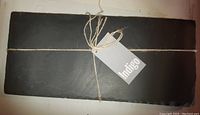 Rectangular dark slate cheese board tied with twine and Indigo brand tag visible.