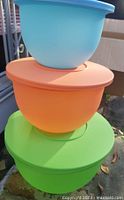 Stacked view of three nesting Tupperware bowls in blue, orange, and green with lids on, showing color and size contrast.