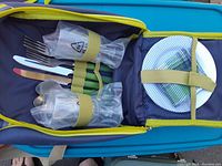 Picnic backpack open to show utensils and plates inside. Items held with elastic straps and mesh pouch.