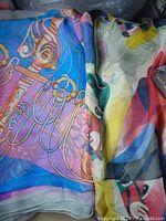 Close-up image of colorful silk scarf with musical instrument motif and adjacent abstract multicolor patterned scarf.