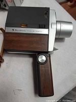 Side angled view of the vintage Bell & Howell Focus-Matic movie camera showing wood paneling and foldable handle