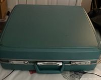 Closed teal vintage Samsonite suitcase with silver locks and handle shown from the front.
