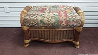 Front view of the wicker bench ottoman showing the woven wicker base and patterned top cushion.