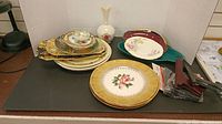 Assortment of plates, stacked and laid out on table, with visible floral designs and gold rims.