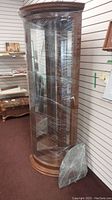 Full frontal view of the tall wood corner cabinet with curved glass front and sides, shrink-wrapped for protection.