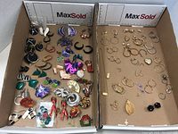 Two cardboard trays displaying assorted earrings, pendants, necklace, keychain and brooch pins