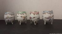 Front view of four porcelain cracked egg vases in pastel blue, green, pink, and blue colors showing the floral and gold detail, each supported by three legs.