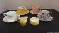 Overhead photo showing all 4 cups with matching saucers, small creamer and sugar bowl, on black background