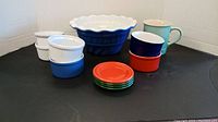 Overview of all items including mugs, small dishes, and large blue bowl on black surface.