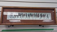 Full view of framed panoramic print showing multiple horses in a snowy birch tree environment with a man leading them, framed in wood with brown matte.