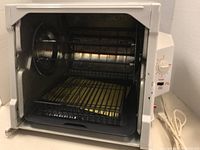 Front view with door open showing rotisserie spit, wire rack, metal basket, and drip tray inside