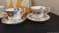Four Royal Albert tea cups and saucers, two shown upright and two shown stacked with undersides visible, showing floral and gold rim design.