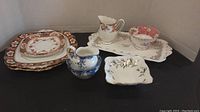 Mixed Royal Albert set including creamers, sugar bowls, small plates, serving tray, and dinner plates displayed on black surface.