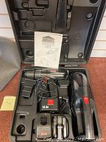 Closed case containing cordless drill with battery, charger, handheld wet/dry vacuum, and instruction manual.