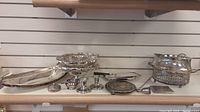 Wide view showing assorted silver-plated serving items including trays, candy dishes, candle sticks, and decorative bowls.