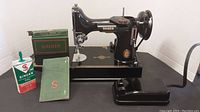 Singer sewing machine set up on black base with oil can, green box, and manual placed alongside