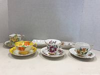 Photo showing four teacups and saucers alongside two small dishes displaying floral designs in various colors and styles.