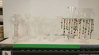 Photo showing a row of clear glass items including vases and candlesticks, two vases decorated with hanging colorful beads, displaying various shapes and sizes.
