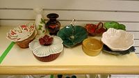 Wide view of assorted colored ceramic bowls, dishes, and vase arranged on a table, showing the full assortment and variety of pieces.