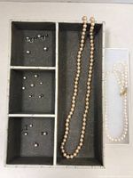 Overall view of the pearl necklaces and earrings organized in a divided jewelry tray, with necklaces in one section and earrings in the others.