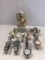 Photo showing all 11 assorted wrist watches arranged around and on a display cone, various metal bands and styles.