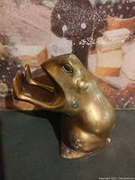 Brass frog statue bookend photographed from front left angle showing open mouth and forelimb.