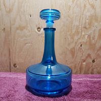 Front view of the blue glass decanter bottle with the stopper in place on top of it.