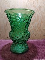 Front view of emerald green textured pressed glass vase with flared top and rounded midsection.