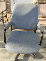 Front view of the used grey fabric office chair showing seat, backrest, and armrests under natural light outside on wooden deck.
